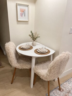 A round dining table with two fluffy chairs, a vase with flowers, and a framed picture on the wall. - Stylish Private 1 bedroom Cozy Suite (Coquitlam)