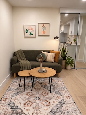 A living room with a sofa, two coffee tables, a rug, and framed artwork on the wall. - Stylish Private 1 bedroom Cozy Suite (Coquitlam)