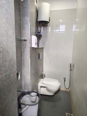 A compact bathroom with a toilet, a shower, and a hand dryer. - HOTEL NARMADA PALACE (Ujjain)