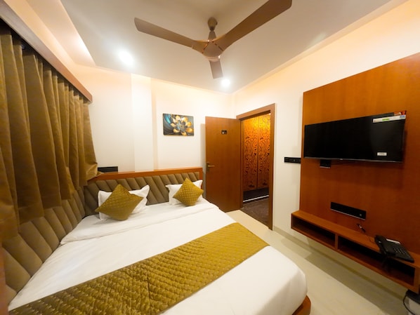 A hotel room with a bed, a ceiling fan, a television, and a door leading to another room. - HOTEL NARMADA PALACE (Ujjain)