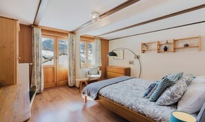 A bedroom with a bed, a chair, a desk, a lamp, and a window with curtains. - TRUDI’S TERRACE – 3-BEDROOM ZERMATT HOME WITH MATTERHORN VIEWS (Zermatt)