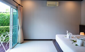A hotel room with a bed, a window with curtains, an air conditioning unit, and a view of greenery outside. - Phuket Rawai Private Pool Villa with Garden - 2BR (Tambon Rawai)