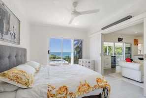A bedroom with a bed, a ceiling fan, and a view of the sea through a sliding door. - Nico’s Butterfly Beach House | Beachfront | 2BR, Sleeps 4 | Spa & Sea Views (Rocky Point)