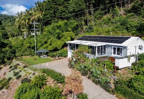 A white house with a solar panel roof, surrounded by lush greenery and a clear sky. - Nico’s Butterfly Beach House | Beachfront | 2BR, Sleeps 4 | Spa & Sea Views (Rocky Point)