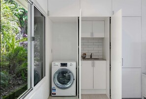 Laundry Area : The laundry area includes a front-loader washing machine, storage cupboards and a compact sink tucked neatly beside the garden outlook. - Nico’s Butterfly Beach House | Beachfront | 2BR, Sleeps 4 | Spa & Sea Views (Rocky Point)