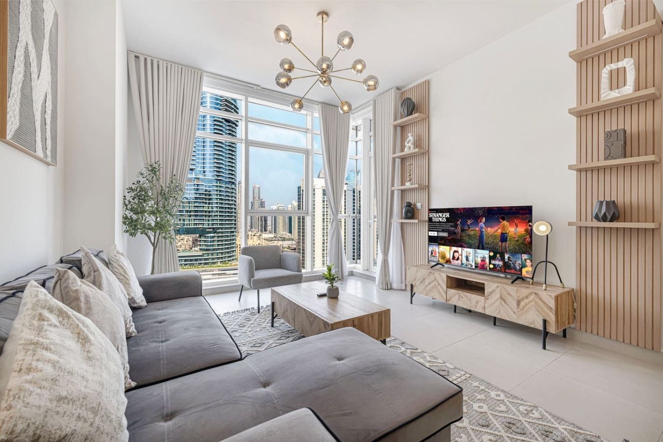 A modern living room with a large flat-screen TV, a sofa set, a coffee table, and a decorative chandelier.