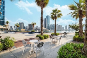 Eine Terrasse im Freien mit Sitzgelegenheiten, Palmen und Blick auf die Stadtlandschaft.