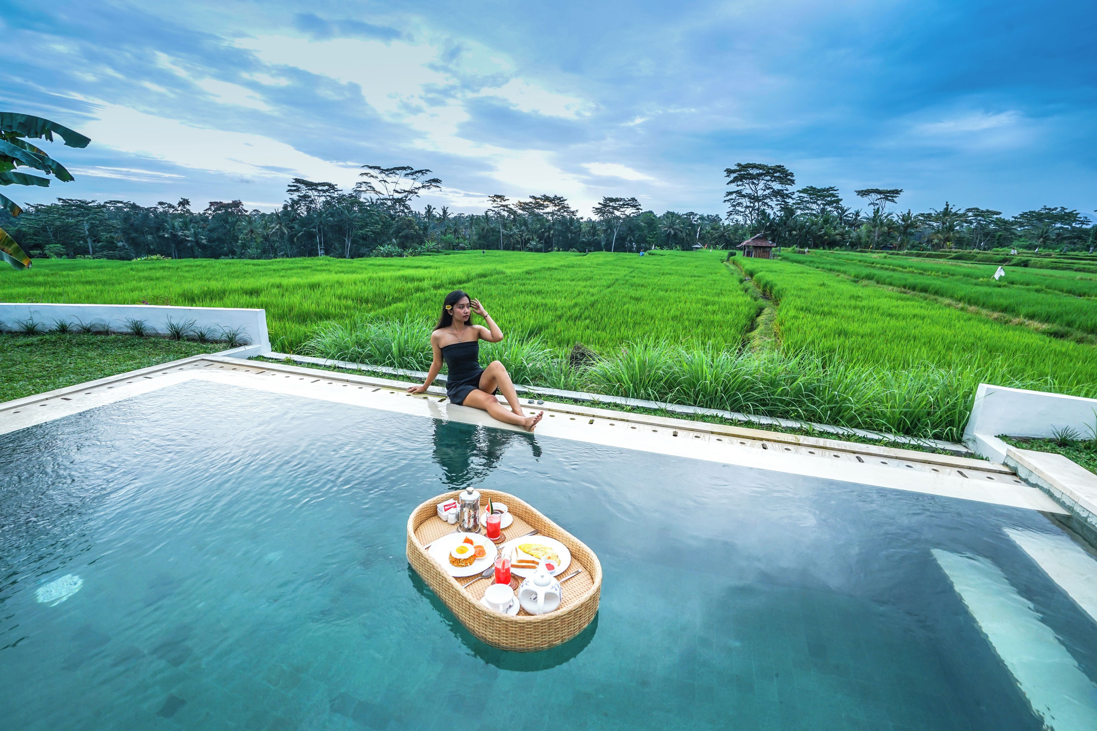Una persona sentada junto a una piscina, con una bandeja de comida flotando.