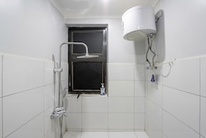 Une petite salle de bain carrelée, équipée d’une douche, d’une fenêtre et de toilettes.