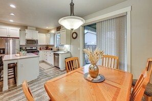 A modern kitchen with white cabinets, a microwave, and a dining area with a wooden table and chairs. - Family Home Close to Bend, Smith Rock & Sisters (Redmond)