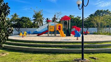 A playground with slides and climbing structures, surrounded by a landscaped area with grass and trees.