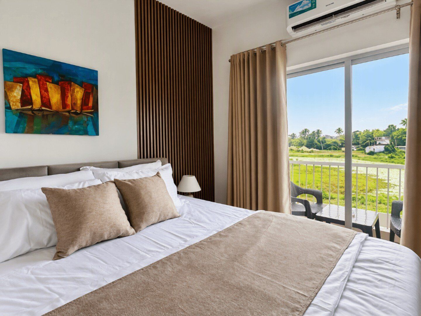 A hotel room with a large bed, a painting on the wall, a window with curtains, and a view of the outdoors.