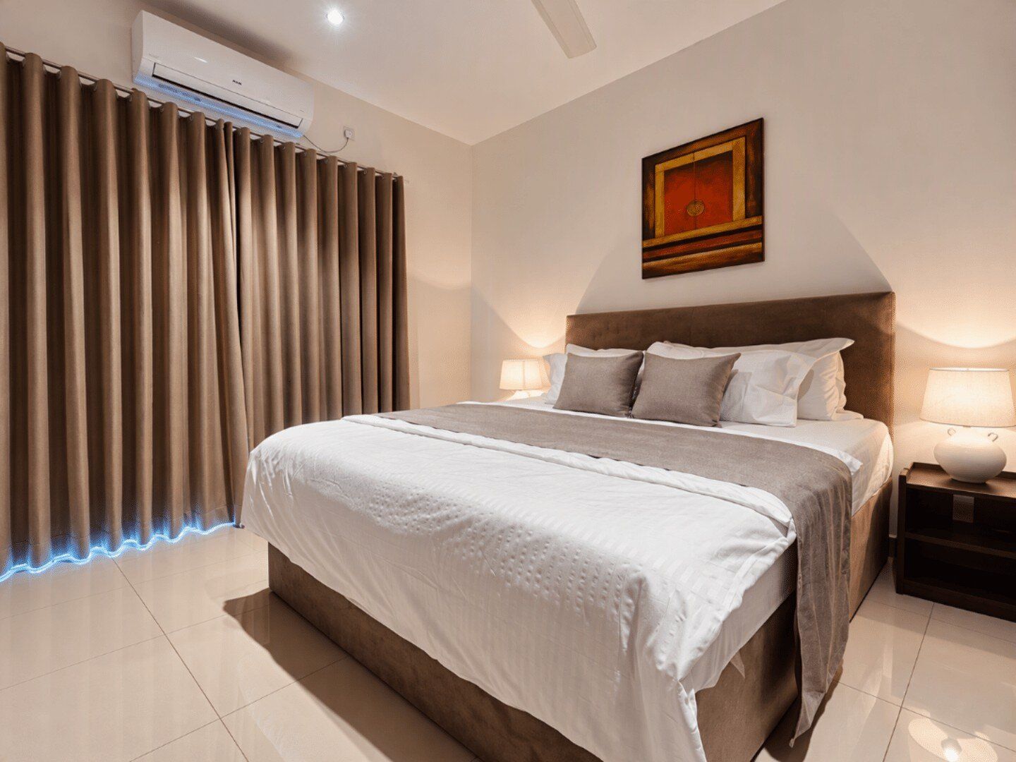 Une chambre d’hôtel moderne avec un grand lit, une table de chevet avec une lampe, un climatiseur fixé au mur et une fenêtre avec des rideaux.