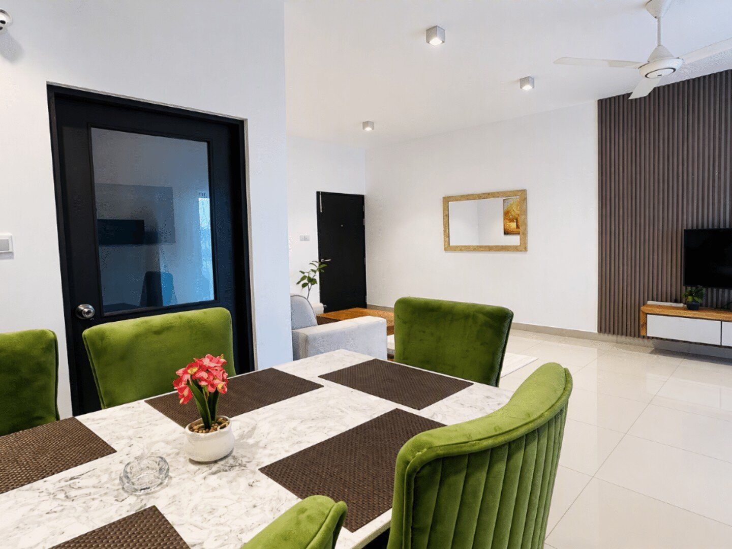 A dining area with a table set for four, green upholstered chairs, and a vase with flowers.