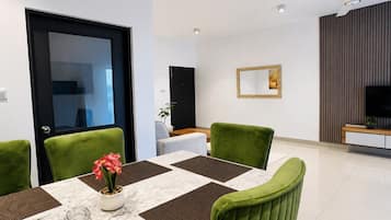 A dining area with a table set for four, green upholstered chairs, and a vase with flowers.