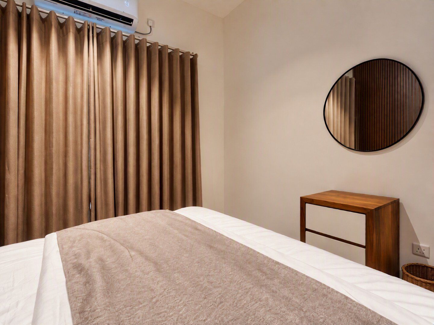 Een hotelkamer met een bed, een nachtkastje, een ronde spiegel en een raam met gordijnen.