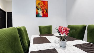 A conference room with a white marble table, green upholstered chairs, a colorful abstract painting on the wall, and a vase with pink flowers.