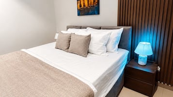 A neatly made bed with a white comforter and several pillows, a bedside lamp, and a wall-mounted painting.