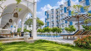 A hotel courtyard with a pool, outdoor seating, and a covered area with umbrellas.