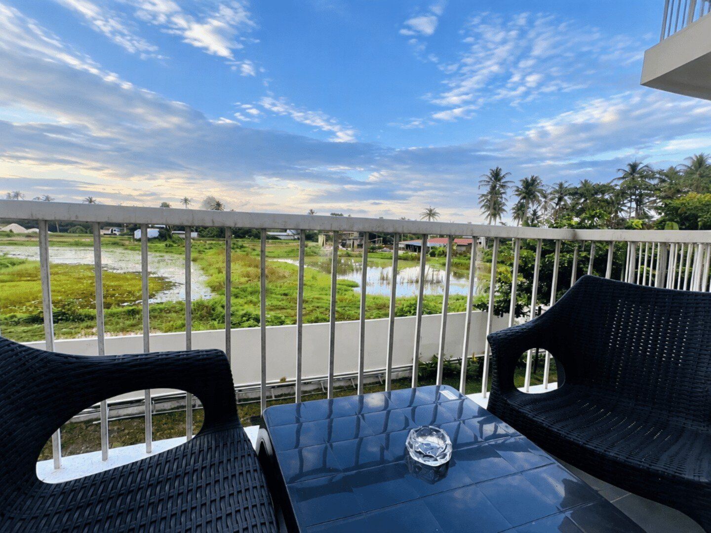 Un balcone con vista su un corpo d'acqua e vegetazione, un tavolo con un bicchiere e due sedie.