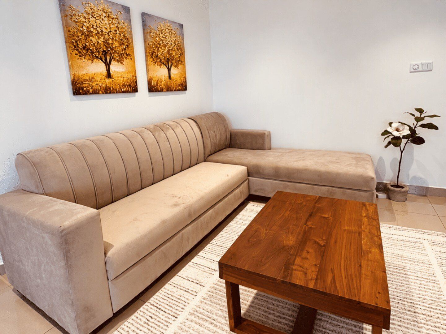 A beige sofa, a wooden coffee table, and two paintings of trees on the wall.