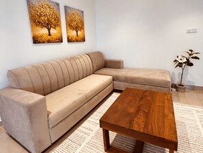 Ein beiges Sofa, ein Holztisch und zwei Baumdarstellungen an der Wand.