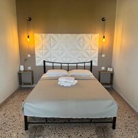 Una cama bien tendida con cabecera de diseño geométrico, dos mesitas de noche con lámparas y un suelo moteado.