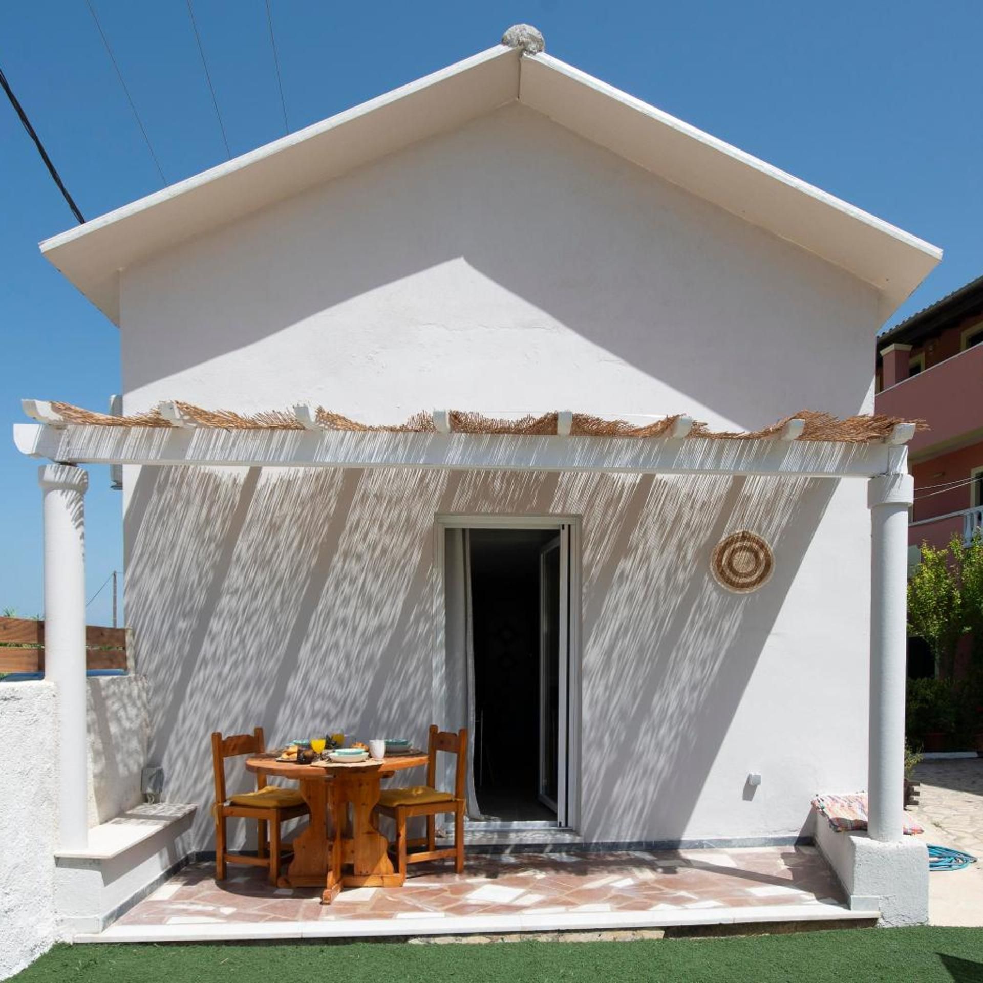 A white building with a covered patio area, a table with chairs, and a door.