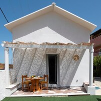 Un edificio blanco con un patio cubierto, una mesa con sillas y una puerta.