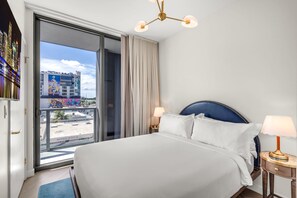 Ein Hotelzimmer mit einem großen Bett, zwei Nachttischlampen, einer Deckenleuchte und Blick auf eine Stadtlandschaft durch eine Schiebetür.