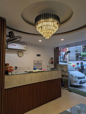 A hotel reception desk with a chandelier, a clock, and a sign for Vajra Hotels.