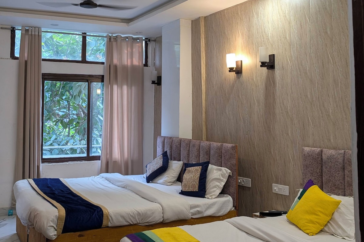 A hotel room with two beds, a ceiling fan, a window with curtains, and a wall-mounted light fixture.