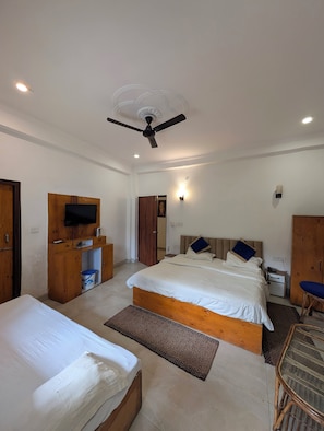 A hotel room with two beds, a television, a ceiling fan, and a small desk with a chair.