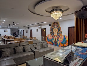 A hotel lobby with a reception desk, seating area, and a large mural. - Vajra Laxmi Narayan Hotel (Rishikesh)