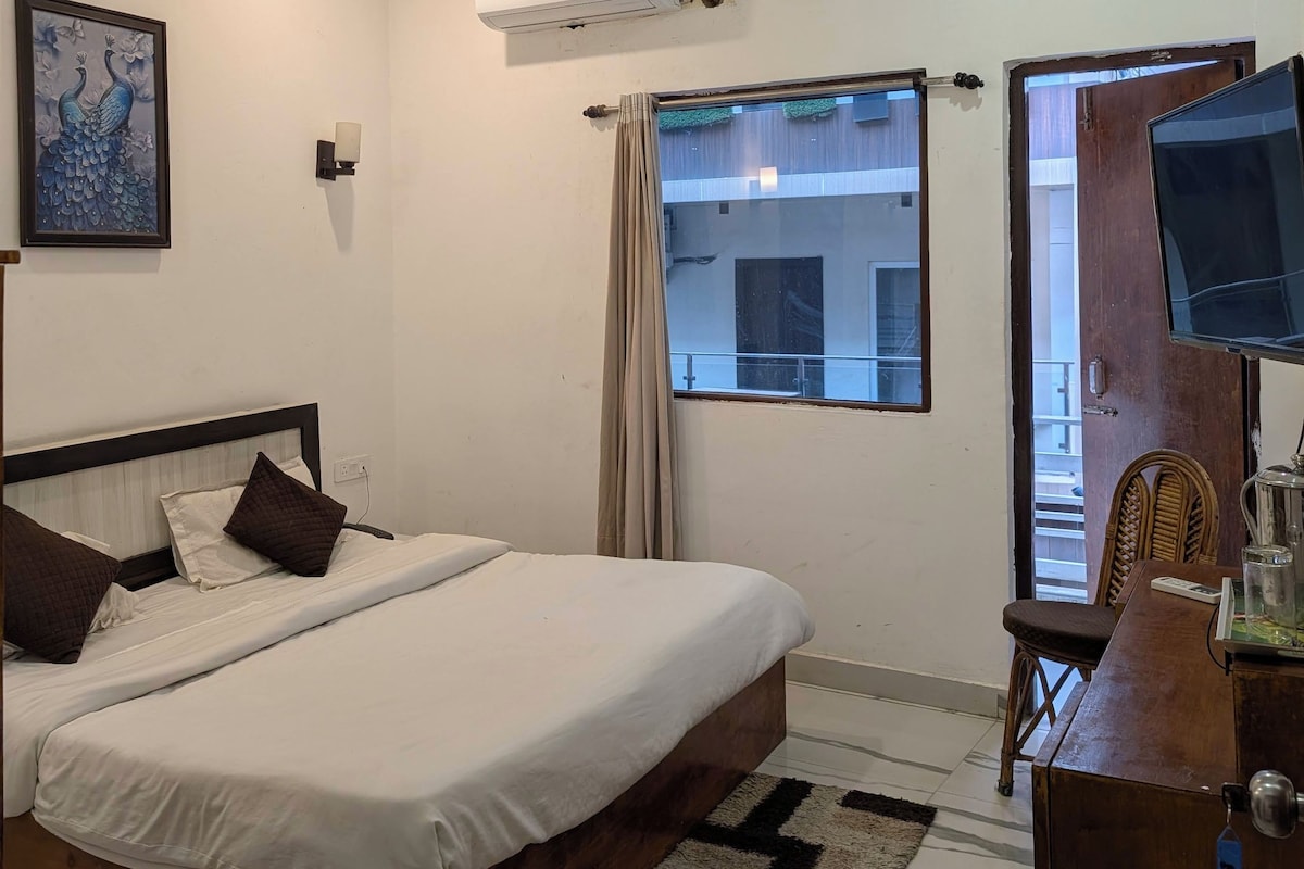 A hotel room with a bed, a ceiling fan, an air conditioning unit, a window with curtains, a television, and a wooden dresser.