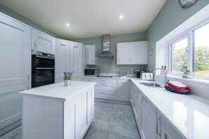 A modern kitchen with white cabinetry, a built-in oven, microwave, and a large window providing a view of greenery outside. - Five Acres - Sleeps 8 - Private Hot Tub - Pet Friendly - Conwy (Conwy)
