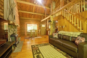 A log cabin interior with a wooden staircase, a leather sofa, and a stone fireplace. - Maine Log Cabin! Private 2.5-Acre Getaway! (Denmark)