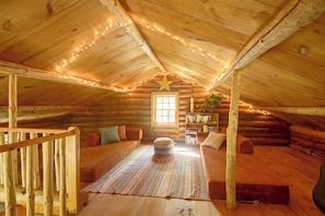 A cozy log cabin interior with a wooden ceiling, string lights, a star decoration, a sofa, a rug, and a bookshelf. - Maine Log Cabin! Private 2.5-Acre Getaway! (Denmark)