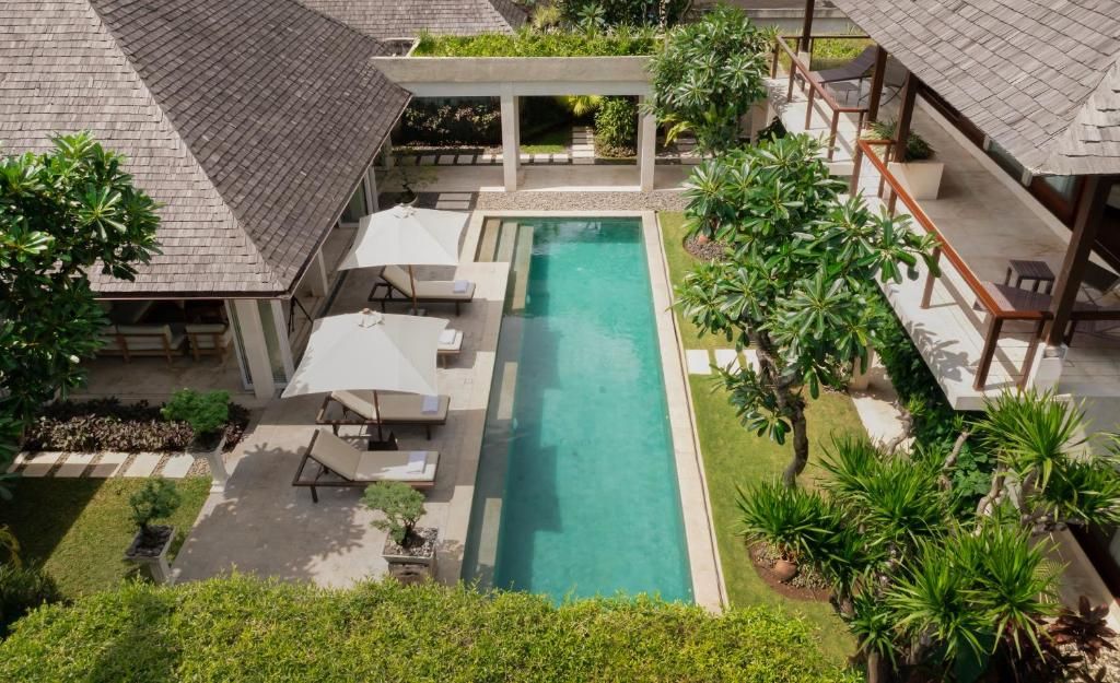 A rooftop pool area with lounge chairs and umbrellas, surrounded by greenery and a covered seating area.