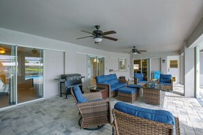 An outdoor patio area with wicker furniture, a barbecue grill, ceiling fans, and a glass door leading to a pool. - Canal-Front Home w/ Boat Lift & Pool in Cape Coral (Cape Coral)
