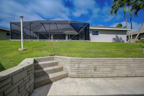 A residential property with a covered outdoor area, a stone retaining wall, and a clear sky. - Canal-Front Home w/ Boat Lift & Pool in Cape Coral (Cape Coral)