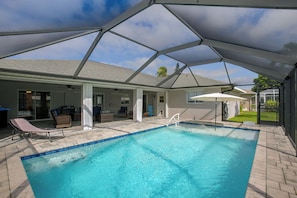 An indoor swimming pool with a clear blue water, surrounded by lounge chairs and a covered patio area. - Canal-Front Home w/ Boat Lift & Pool in Cape Coral (Cape Coral)