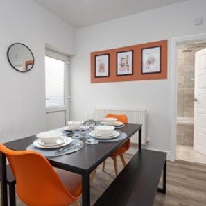 A dining area with a black table, orange chairs, and framed pictures on the wall. - Central Bishop Auckland - Stay 5 - Transport Links (Bishop Auckland)