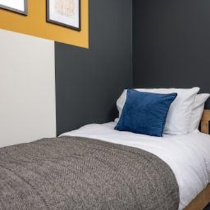 A bed with white bedding and a blue pillow, a gray throw blanket, and a dark wall with a framed picture above it. - Central Bishop Auckland - Stay 5 - Transport Links (Bishop Auckland)