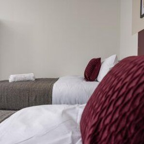 A hotel room with two beds, a white wall, and a red accent pillow. - Central Bishop Auckland - Stay 5 - Transport Links (Bishop Auckland)
