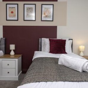 A neatly made bed with a white comforter and a red throw pillow, a bedside table with a lamp, and a framed picture on the wall. - Central Bishop Auckland - Stay 5 - Transport Links (Bishop Auckland)