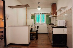 A compact kitchen with a refrigerator, a microwave, and a sink. There is a dining table with chairs and a window with curtains. - Wine Aparts (Mendoza)