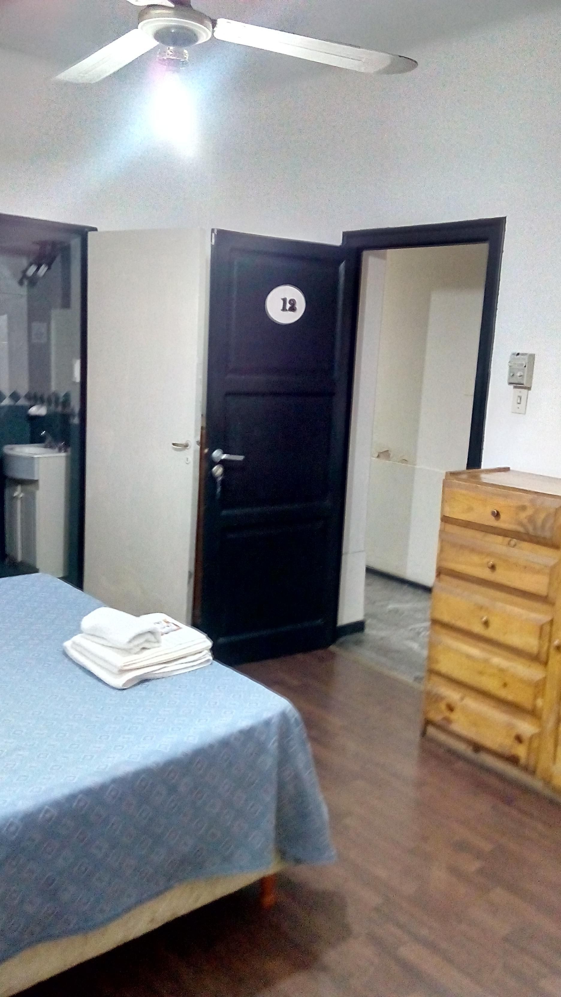 A bedroom with a bed, a dresser, a door with a number, and a ceiling fan.