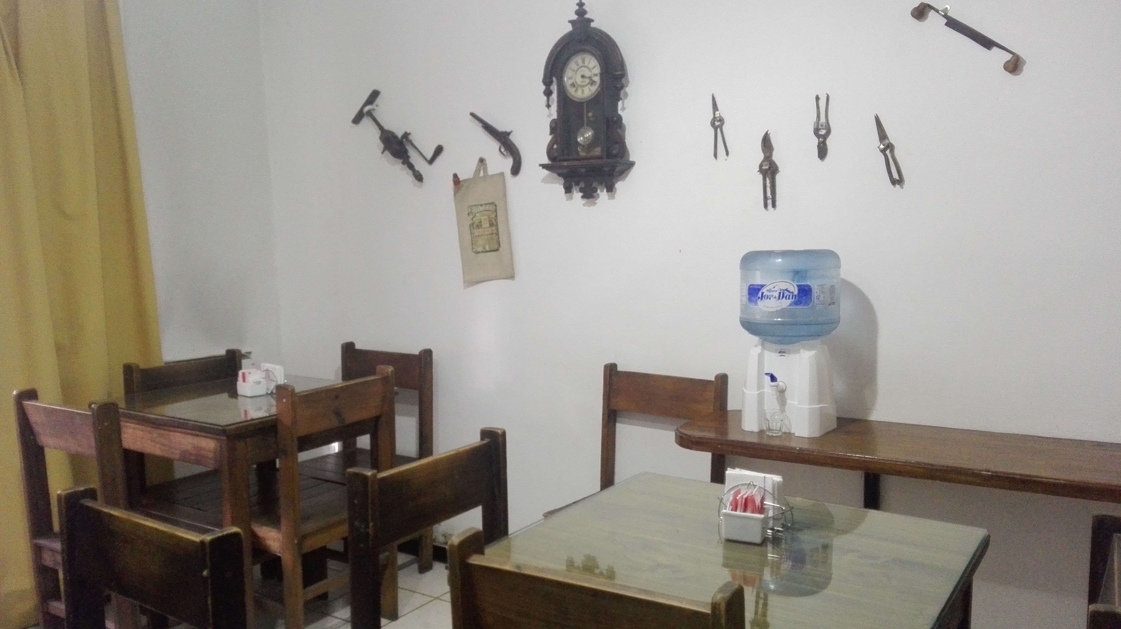 Un comedor con sillas de madera y una mesa, un dispensador de agua y herramientas fijadas a la pared.
