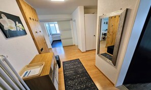 A hallway with a wooden floor, a black rug, a mirror, and a door leading to a room. - CENTRAL ZERMATT APARTMENT WITH STUNNING MATTERHORN VIEWS (Zermatt)